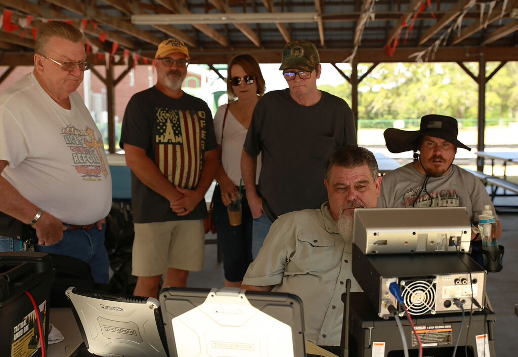 Mark Dawkins, N4CMD, working amateur radio while others look on at club field day, 2024.