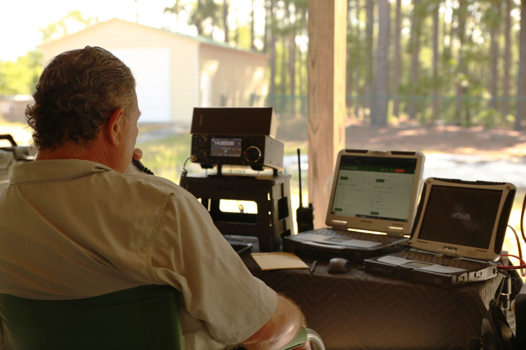 Mark Dawkins, N4CMD, working amateur radio while others look on at club field day, 2024.